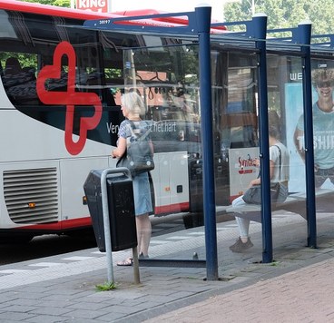 dame met grijs haar staat bij bushalte waar de bus voorrijdt